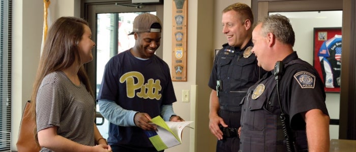 two individuals speaking to two police officers in uniform, all individuals are smiling